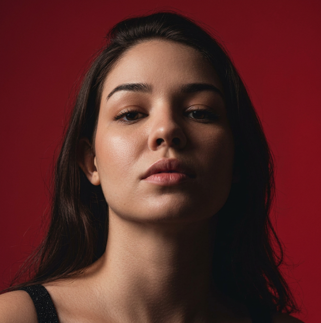 Retrato de uma mulher com cabelo escuro, olhando diretamente para a câmera, com um fundo vermelho.